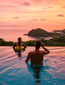 a young couple of men and women at a swimming pool during a vacation on a tropical island. man and woman in infinity pool during sunset. luxury vacation in Thailand pool of a luxury pool villa