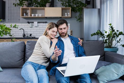 Married couple man and woman sitting together at home on the couch using laptop for video chat and chatting with friends
