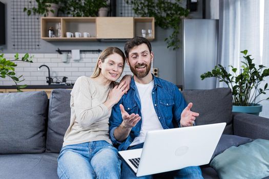 Married couple man and woman sitting together at home on the couch using laptop for video chat and chatting with friends