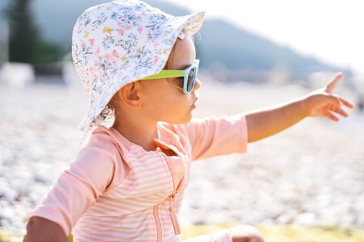 Little girl in sunglasses on the beach pointing her finger into the distance. High quality photo