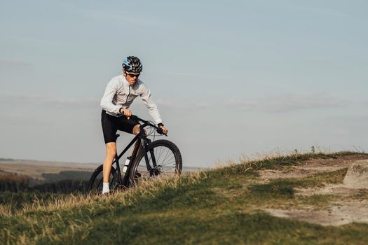 Equipped Professional Male Cyclist Riding Mountain Bike on Top of Hill, Copy Space on Sky Background