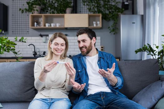 Happy couple man and woman on the couch sitting and rejoicing in a positive pregnancy test