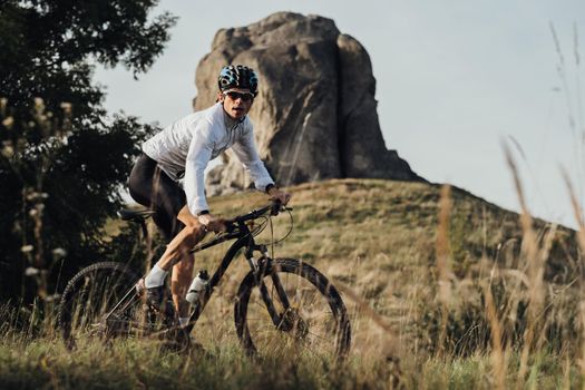 Professional Equipped Cyclist on Trail with Giant Stone, Miracle of Nature on Background, Adult Man Riding Bike Outdoors