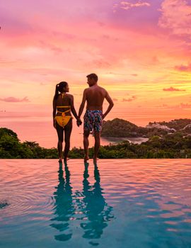 a young couple of men and women at a swimming pool during a vacation on a tropical island. man and woman in infinity pool during sunset. luxury vacation in Thailand pool of a luxury pool villa