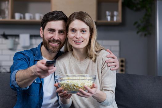 Photo of close couple man and woman together at home having fun and happily watching TV and eating popcorn
