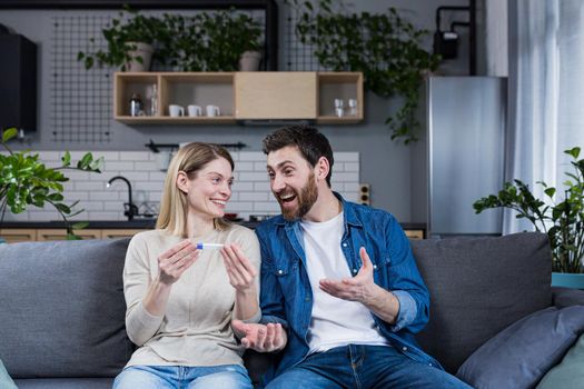 Happy couple man and woman on the couch sitting and rejoicing in a positive pregnancy test