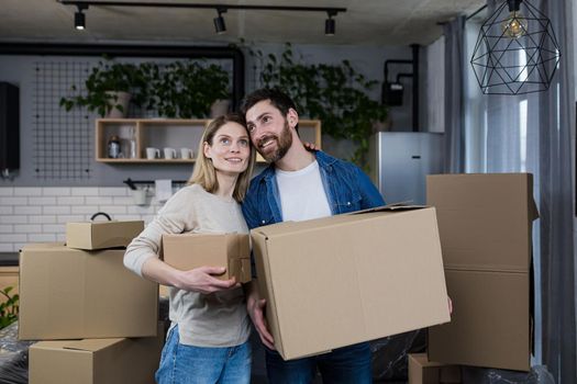 Happy couple man and woman live together, moved to a new rented apartment, holding cardboard boxes