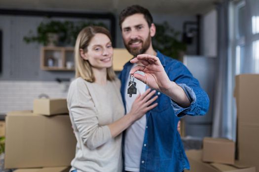 Selected focus, married couple man and woman happy together, hugging, holding the keys to their new apartment, housewarming, close-up photo