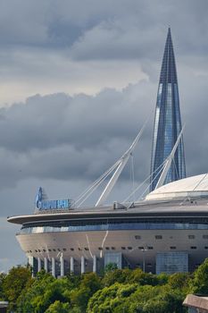 Russia, St. Petersburg, 29 July 2022: The new building of football stadium Gazprom Arena, the sliding metal roof glitters with spires in the sun, the skyscraper Lakhta for the gas company Gazprom. High quality photo