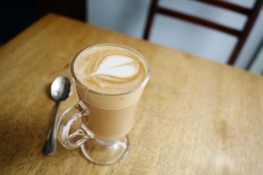 a cup of late coffee with flower shape design on top at cafe .