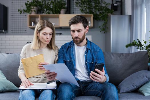 Thoughtful man and woman, pay bills at home, use the application on the phone, serious about paperwork