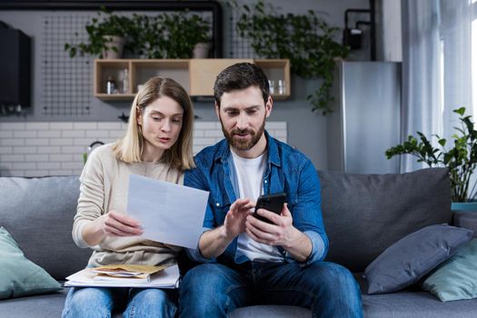 Thoughtful man and woman, pay bills at home, use the application on the phone, serious about paperwork