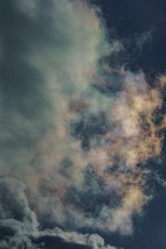 Diffraction of light on drops of supercooled water in clouds, rainbow clouds against the blue sky in clear sunny weather, irisation of cumulus clouds, optical phenomenon, spectral colors. High quality photo