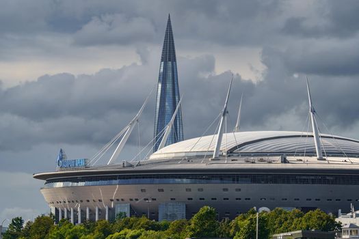 Russia, St. Petersburg, 29 July 2022: The new building of football stadium Gazprom Arena, the sliding metal roof glitters with spires in the sun, the skyscraper Lakhta for the gas company Gazprom. High quality photo