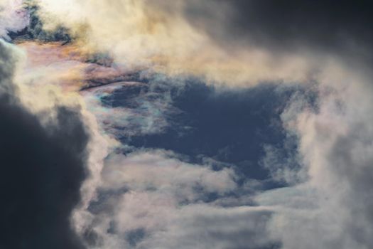 Diffraction of light on drops of supercooled water in clouds, rainbow clouds against the blue sky in clear sunny weather, irisation of cumulus clouds, optical phenomenon, spectral colors. High quality photo