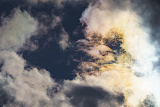 Diffraction of light on drops of supercooled water in clouds, rainbow clouds against the blue sky in clear sunny weather, irisation of cumulus clouds, optical phenomenon, spectral colors. High quality photo