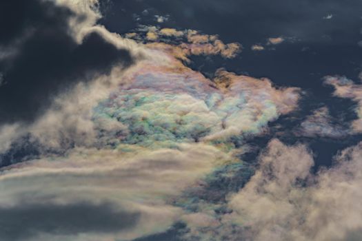 Diffraction of light on drops of supercooled water in clouds, rainbow clouds against the blue sky in clear sunny weather, irisation of cumulus clouds, optical phenomenon, spectral colors. High quality photo