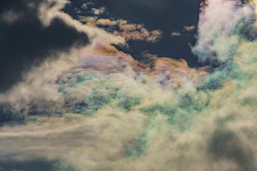 Diffraction of light on drops of supercooled water in clouds, rainbow clouds against the blue sky in clear sunny weather, irisation of cumulus clouds, optical phenomenon, spectral colors. High quality photo