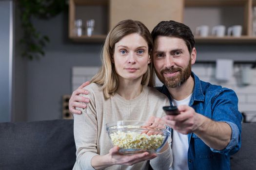 Photo of close couple man and woman together at home having fun and happily watching TV and eating popcorn