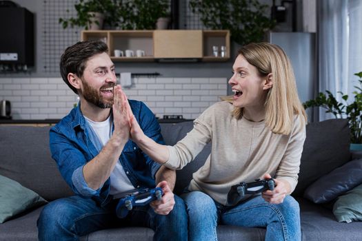 Happy couple man and woman playing game using joystick while sitting on sofa at home