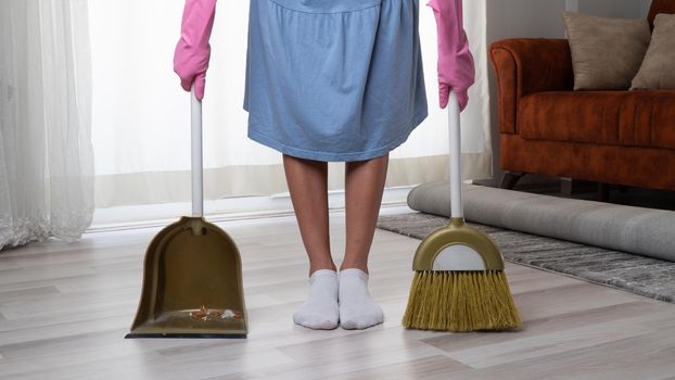 A housewife in rubber pink gloves stands between a broom and a scoop when cleaning the apartment. High quality photo