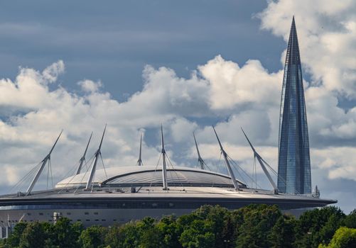 Russia, St. Petersburg, 29 July 2022: The new building of football stadium Gazprom Arena, the sliding metal roof glitters with spires in the sun, the skyscraper Lakhta for the gas company Gazprom. High quality photo