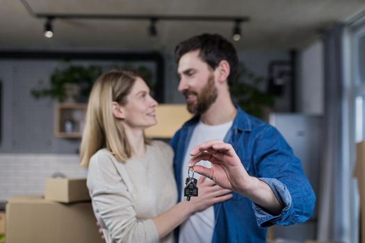 Selected focus, married couple man and woman happy together, hugging, holding the keys to their new apartment, housewarming, close-up photo