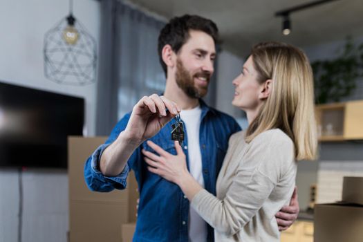 Selected focus, married couple man and woman happy together, hugging, holding the keys to their new apartment, housewarming, close-up photo