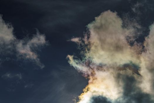 Diffraction of light on drops of supercooled water in clouds, rainbow clouds against the blue sky in clear sunny weather, irisation of cumulus clouds, optical phenomenon, spectral colors. High quality photo