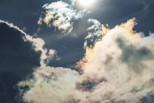 Diffraction of light on drops of supercooled water in clouds, rainbow clouds against the blue sky in clear sunny weather, irisation of cumulus clouds, optical phenomenon, spectral colors. High quality photo