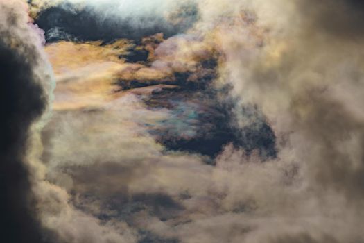 Diffraction of light on drops of supercooled water in clouds, rainbow clouds against the blue sky in clear sunny weather, irisation of cumulus clouds, optical phenomenon, spectral colors. High quality photo