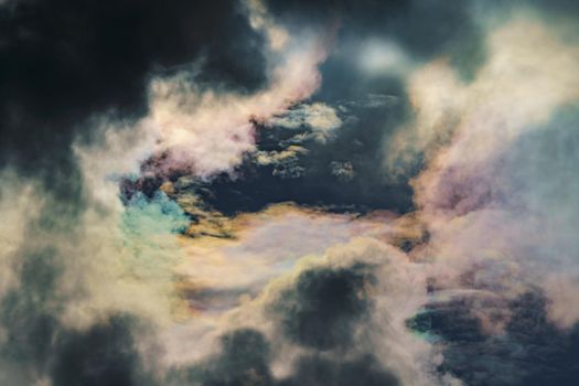 Diffraction of light on drops of supercooled water in clouds, rainbow clouds against the blue sky in clear sunny weather, irisation of cumulus clouds, optical phenomenon, spectral colors. High quality photo