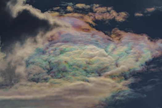 Diffraction of light on drops of supercooled water in clouds, rainbow clouds against the blue sky in clear sunny weather, irisation of cumulus clouds, optical phenomenon, spectral colors. High quality photo