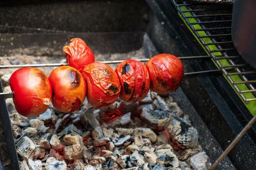 Ripe fresh tomatoes are grilled on a skewer over hot coals. Selective focus.