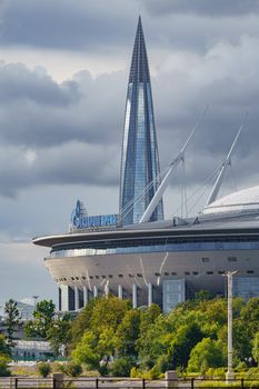 Russia, St. Petersburg, 29 July 2022: The new building of football stadium Gazprom Arena, the sliding metal roof glitters with spires in the sun, the skyscraper Lakhta for the gas company Gazprom. High quality photo