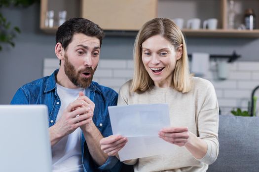 Happy married couple, man and woman, received a positive letter, sitting at home on the couch, smiling and rejoicing