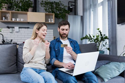 Online shopping. Man and woman shopping online from a notebook, holding a credit card in his hands. A purchase for a woman she chose herself. At home, sitting on the couch. Happy, satisfied