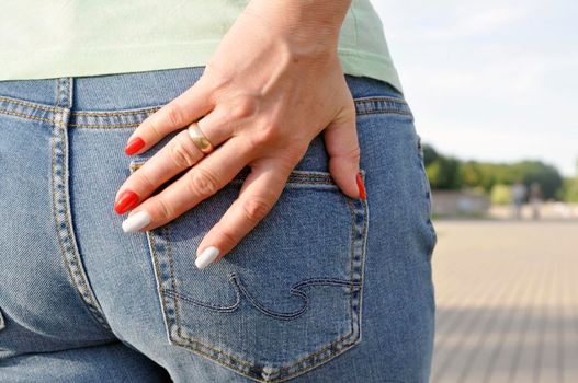 Woman's hand with a perfect manicure on denim trousers from behind. Red and white.
