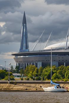 Russia, St. Petersburg, 29 July 2022: The new building of football stadium Gazprom Arena, sailing and motor boats are moored near embankment, the skyscraper Lakhta for the gas company Gazprom. High quality photo