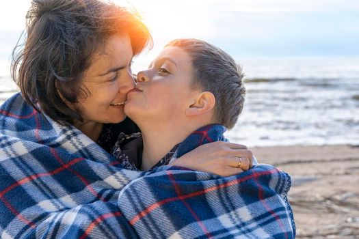 a happy mother and her preschooler son are relaxing on the beach wrapped in a plaid plaid from the wind in the light of the setting sun. parental love. family ties. Mother's Day