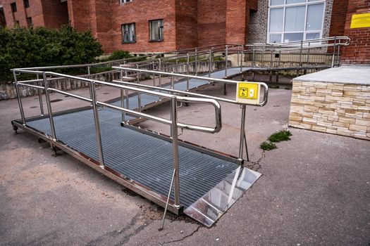 A ramp and a call button for people with disabilities near a public building. Iron ramp for the disabled at the entrance to the city library