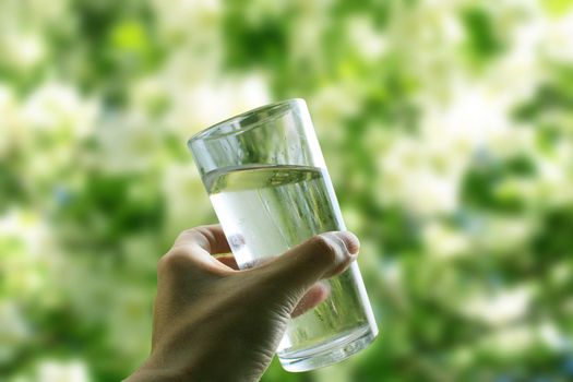 A glass of water in a hand close-up on a natural green background outdoors..