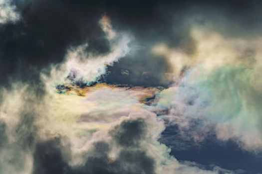Diffraction of light on drops of supercooled water in clouds, rainbow clouds against the blue sky in clear sunny weather, irisation of cumulus clouds, optical phenomenon, spectral colors. High quality photo