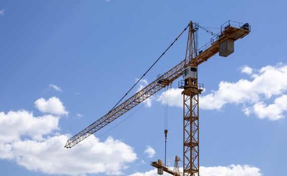 A working construction tower crane against a cloudy sky on a sunny day. The concept of urban development and construction. Industrial background. Crane engineering, construction industry tool