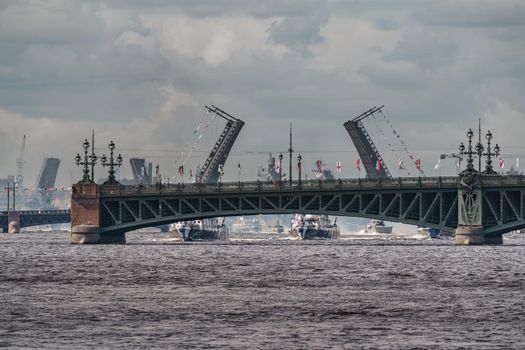 Russia, St. Petersburg, 28 July 2022: A lot of warships goes along the Neva River under open bridges at the time of the rehearsal of the celebration of the day of the Navy in sunny weather. High quality photo