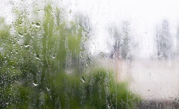 Heavy rain. Raindrops on the window glass on a summer day. Selective focus, shallow depth of field. Drops of water fall on a wet window. Glass full of drops during a downpour