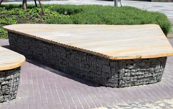 Wooden benches from gabion baskets with stones inside. Wood mounted on gabions. Benches of modern design. Detail of a low wood-topped gabion wall for use as a bench