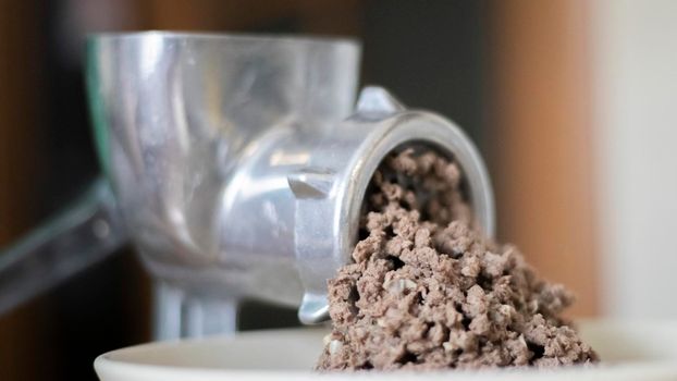 Minced meat in a manual mechanical meat grinder. Fresh boiled meat is ground with an old metal meat grinder, close-up in the kitchen