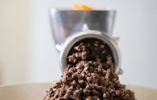 Minced meat in a manual mechanical meat grinder. Fresh boiled meat is ground with an old metal meat grinder, close-up in the kitchen
