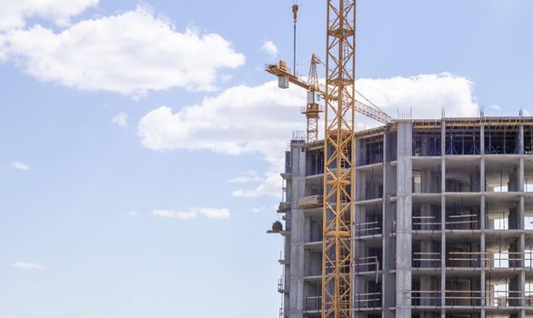 A working construction tower crane against a cloudy sky on a sunny day. The concept of urban development and construction. Industrial background. Crane engineering, construction industry tool